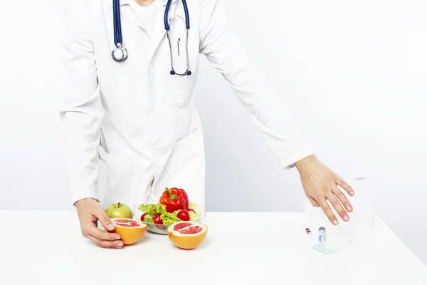 young pretty doctor with stethoscope holding fruits, vegetables and pills, syringe, healthy food care concept