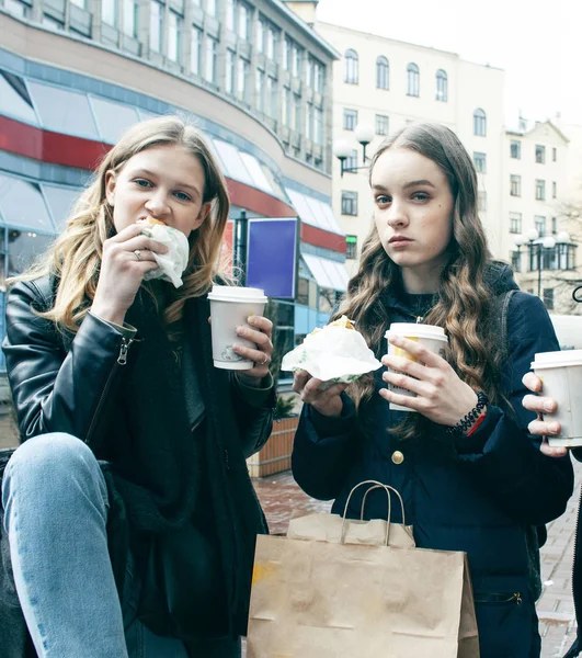 lifestyle and people concept: two girls and guy eating fast food on city street together having fun, drinking coffee