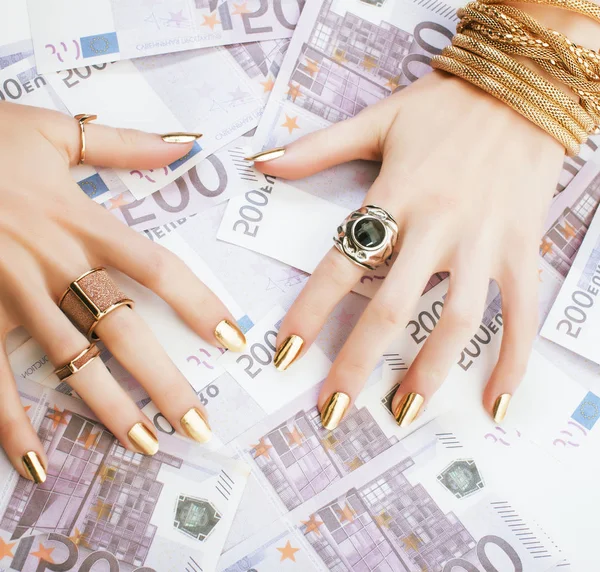hands of rich woman with golden manicure and many jewelry rings on cash euros