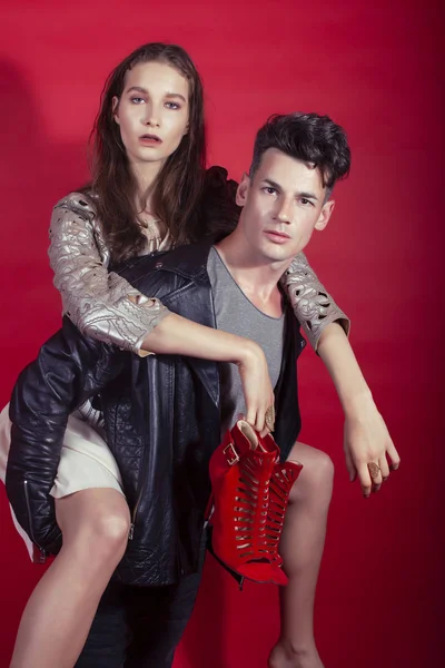young pretty guy and girl closed in fashion style after party shoes in hand posing on red background, lifestyle people concept