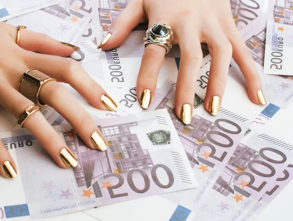 hands of rich woman with golden manicure and many jewelry rings on cash euros