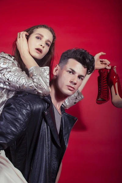 young pretty guy and girl closed in fashion style after party shoes in hand posing on red background, lifestyle people concept