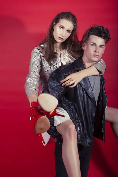 young pretty guy and girl closed in fashion style after party shoes in hand posing on red background, lifestyle people concept