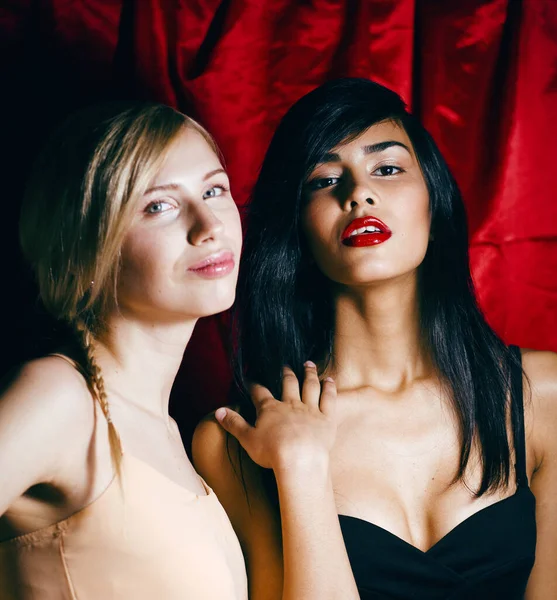 brunette and blond woman together friends on red background, conflict of types