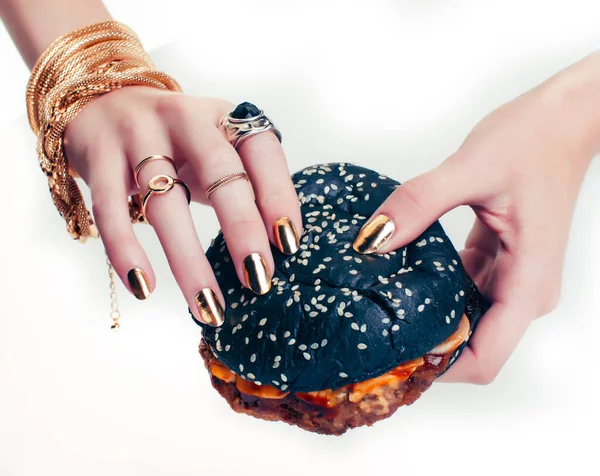 hands of rich woman with golden manicure and jewelry holding black hamburger closeup fashion concept