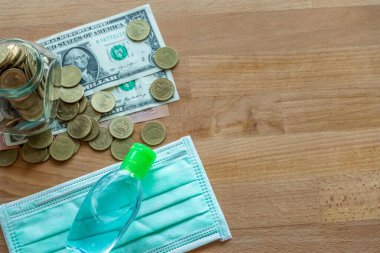 Masadaki madeni paralar ve yüz maskesi ve el temizleme jeli gibi dolar banknotları. Corona virüsü salgını sırasında pahalı yüz maskesi ve fotokopi alanı ile el jeli..