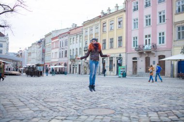 Kasaba meydanındaki kızıl saçlı kız eski binaların arka planında eğleniyor.