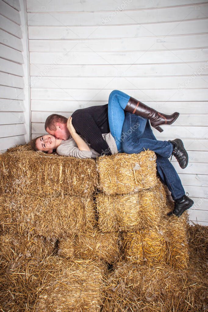 Guy with a girl kissing on bales of hay in the barn.