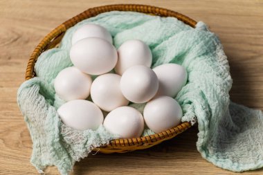 Hasır sepetteki beyaz yumurtalar ve nane bezi. Hafif ahşap arka planda yumurtalar