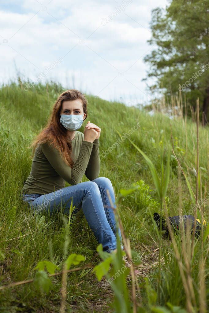 A girl in a mask is sitting on the green grass.