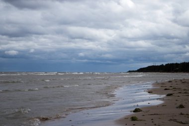 Kumlu sahil, bulutlu hava ve güçlü dalgalar.
