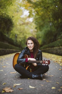 Güzel ve genç birbayan ormanın üzerinde oturan gitar çalmak.