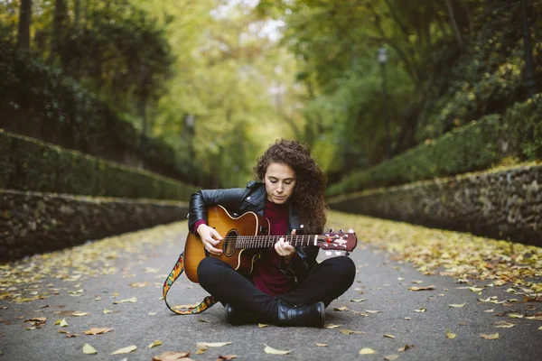 Piękna młoda kobieta gra na gitarze, siedząc w lesie. — Zdjęcie stockowe