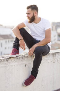 Duvarda oturan sakallı adam.