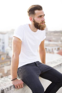 Duvarda oturan sakallı adam.