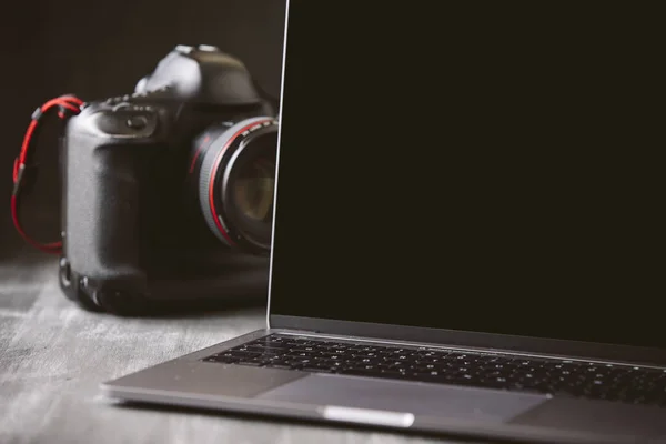 Laptop and a camera on a dark wooden background.