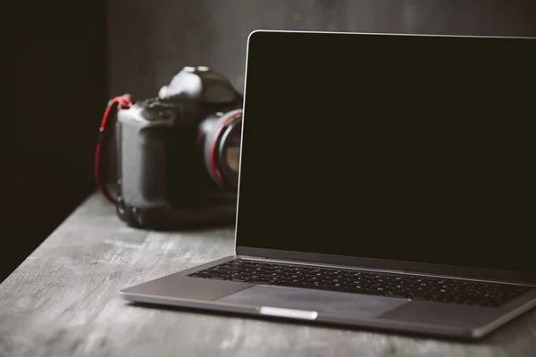 Laptop and a camera on a dark wooden background.