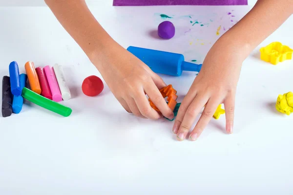 Маленькая рука ребенка научиться играть цветные тесто на белом столе — стоковое фото