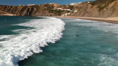 Portekiz, Algarve 'deki bir uçurumun kenarındaki beyaz suda yüzen sörfçülerin insansız hava aracı görüntüleri..