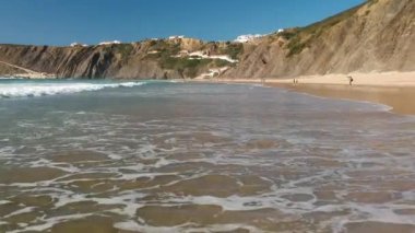 Portekiz, Algarve 'deki bir uçurumun kenarındaki sahilde uçan beyaz su dalgalarının insansız hava aracı görüntüleri..