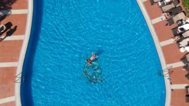 Bir otelin havuzunda yüzen ve gökyüzüne bakan bir adamın insansız hava aracı görüntüleri..