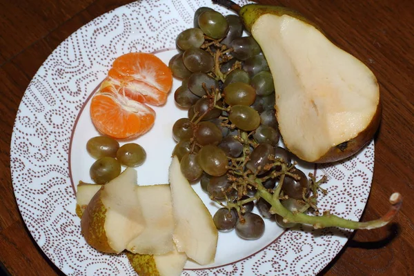 Fruit plate. On a white plate are green grapes, tangerine, and sliced pears. fruit diet and healthy lifestyle