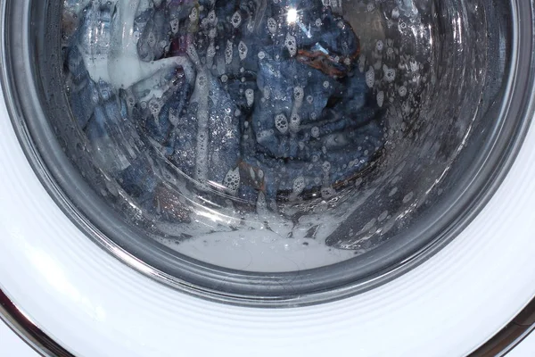 Linen and clothes is washed in a drum washing machine. Soapy water, foam and bubbles. Domestic life.