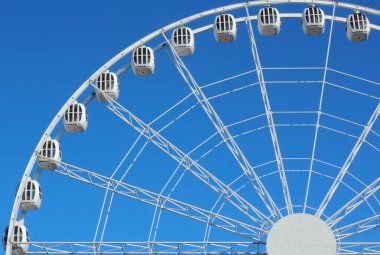 Güneşli bir bahar gününde bulutsuz mavi gökyüzüne karşı büyük beyaz bir dönme dolap.