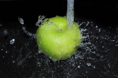 Yeşil elma siyah arka planda akan bir su akıntısının altında yıkanır. Su damlaları ve su damlaları birbirinden uçar..