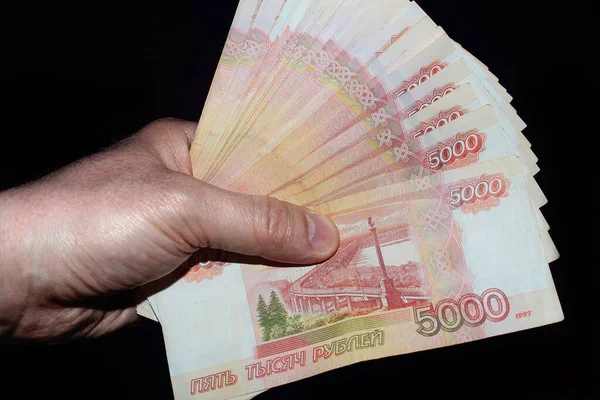 the money is fanned out in my hand. Russian rubles in banknotes of five thousand rubles in red and white colors on a black background