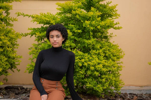 Schöne Frau mit lockigem Haar sitzt mit grünem Baum im Hintergrund — Stockfoto