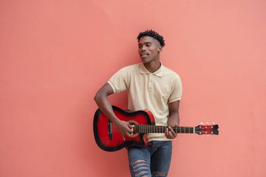 Genç adam parlak renkli duvara karşı gitar çalıyor.