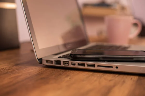 Mobieltje en laptop op houten bureau met wazig kopje op de achtergrond — Stockfoto
