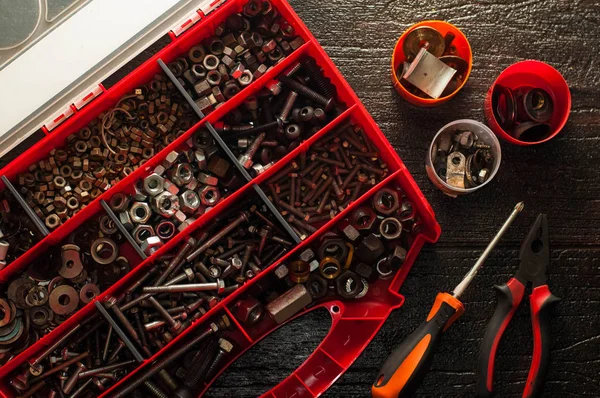 Red boxes with details. nuts, bolts, clamps, hardware. Near screwdriver and pliers — Stock Photo, Image