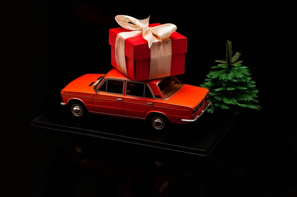 Modelo de um carro vermelho com um presente no telhado. Em um fundo preto com uma pequena árvore de Natal . — Fotografia de Stock