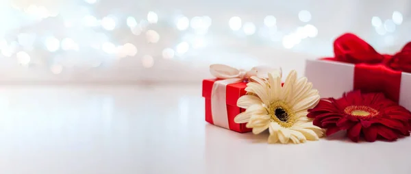 Red gift boxes with ribbons and flowers on a white delicate background with bokeh.