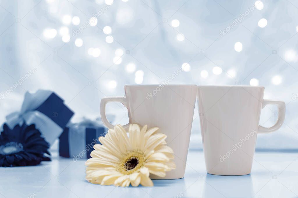 classic blue gift boxes with ribbons, a pair of white cups and flowers on a white delicate background with bokeh.
