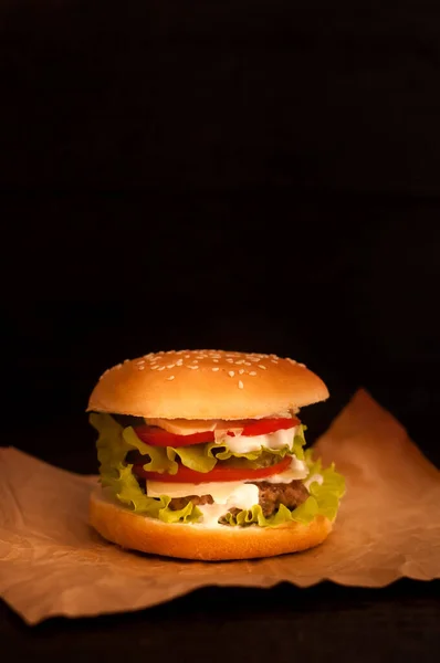 American burgers on tracing paper or food paper with tomatoes on a dark background