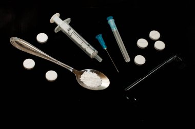 Siyah arka planda beyaz tabletler ve şırıngalar. Kaşıkta toz. Uyuşturucular ve AIDS 'in sonuçları