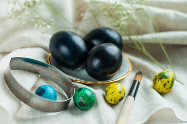 Altın kenarlı bir tabakta siyah yumurtalar ve yanında gri keten arka planda çok renkli bıldırcın yumurtaları. yatay resim