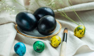 Altın kenarlı bir tabakta siyah yumurtalar ve yanında gri keten arka planda çok renkli bıldırcın yumurtaları. yatay resim