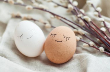 Yüzü olan beyaz ve kırmızı Paskalya yumurtası. Yanında gri keten bir arka planda söğüt dalı var.