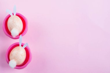 İki Paskalya yumurtası tavşanı pembe ve beyaz arka planda pembe bir kek kalıbının içinde otururlar.