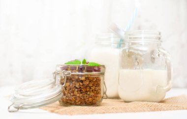 Sağlıklı ve düzgün beslenme kavramı. Kavanozda süt, saplı granola, bir kavanozda nane yaprağı ve kızılcıklı peçete.
