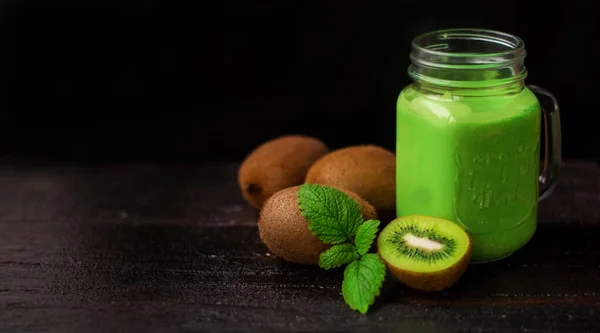 yeşil ferahlatıcı kivi smoothie içinde naneli ve saplı bir kavanoz. İleride kivi meyvesi ve nane yaprağı var.