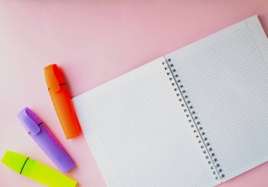 Pembe arka planda bir kafesin içinde açık bir defter. Klavye düzeni. Ofis malzemelerinin yanında. Bir kız için iş konsepti ya da okula dönüş.