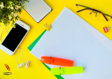 Sarı arka planda boş ekranlı telefon, beyaz elektrikli süpürge kulaklıklar, not defteri, ataçlar ve diğer ofis malzemeleri. Model yap. Kopyalama alanı olan pankart. İş konsepti ya da okula dönüş.