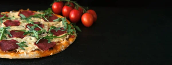 Koyu kırsal bir zeminde, domates ve roka yeşilliklerinin yanında ev yapımı pizza. Metin için yeri olan uzun pankart