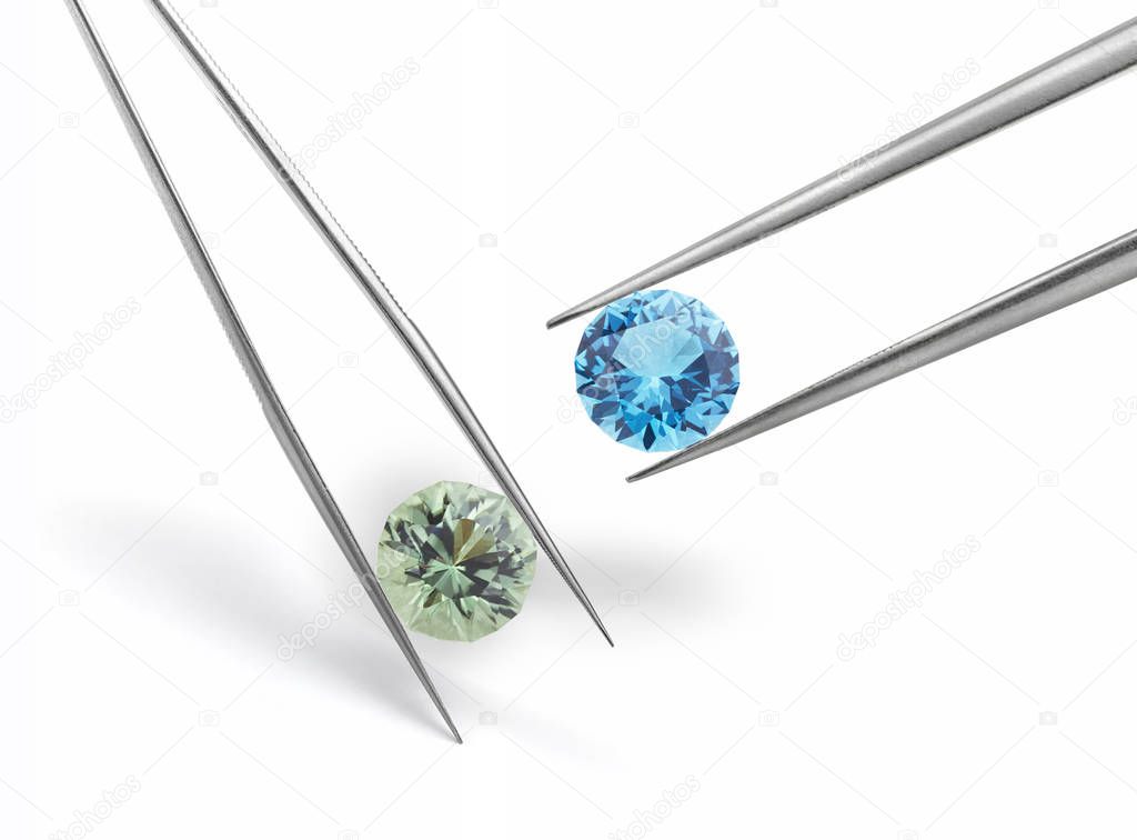 Blue and Green Coloured Gemstones Held in Tweezers on White Background