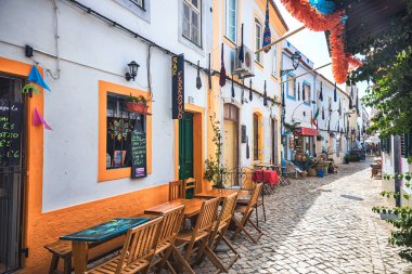 Portekiz 'in Algarve bölgesindeki Ferragudo köyünün asfaltlı bir sokağındaki restoranların terasları.